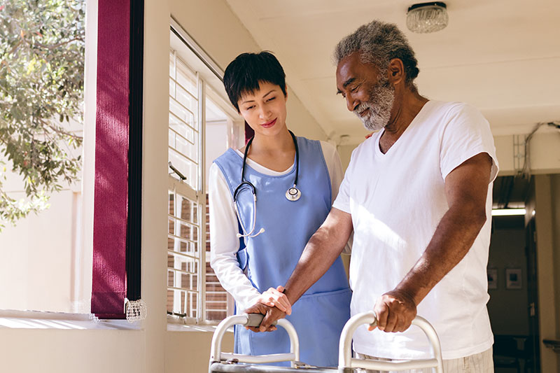 A nurse assisting an elderly African American man using a walker 